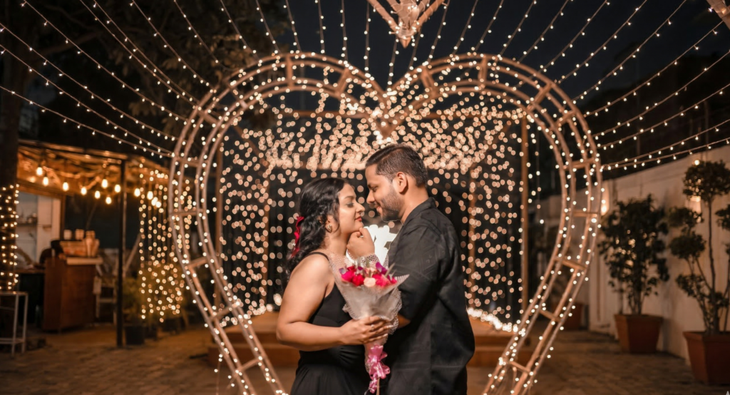 Romantic pre wedding shoot in Jaipur with couple standing under heart shaped light decoration holding bouquet during night photoshoot