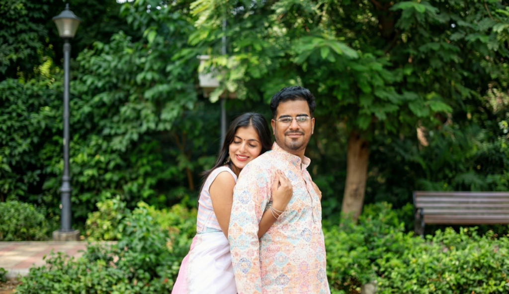A couple during a pre-wedding shoot in Delhi, with the woman leaning on the man's shoulder in a lush green park, captured by Vishal Photos.