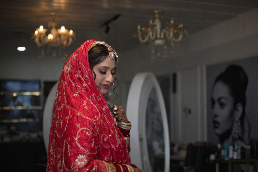 Elegant Indian bride in red bridal lehenga with gold embroidery, posing indoors during a bridal photoshoot in Jodhpur with soft lighting and royal ambiance.