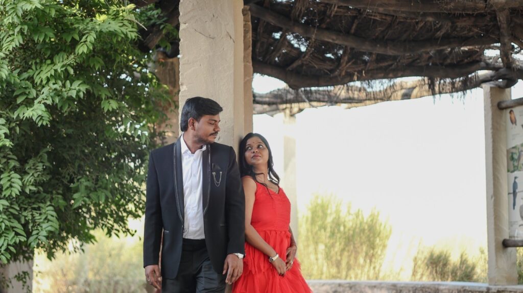 Romantic pre wedding photoshoot of a couple under a rustic wooden pavilion in Jodhpur, featuring elegant red gown and formal attire